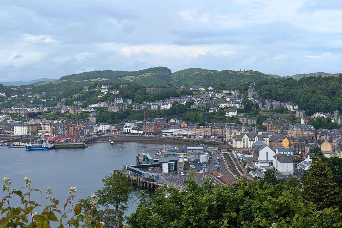 View down towards Oban with the ferry terminal and station closest. The tower is on the hill behind surrounded by trees. 