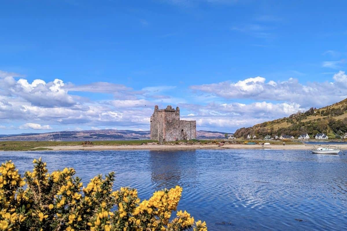 A small ruined fortress on a sandy strip behind a blue loch. The Isle of Arran in Scotland. 