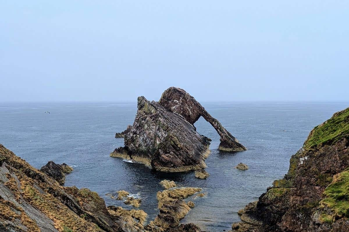 A large rock with a natural arch lies in the grey water. Bow Fiddle Rock on the Moray Coast. 