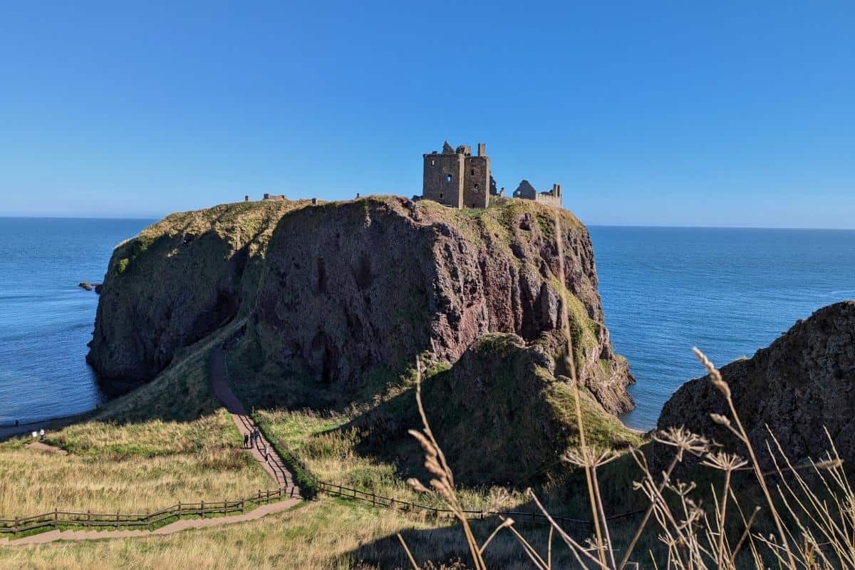 A castle ruin on a grassy mound framed against the blue sea. Dunnottar Castle in Aberdeenshire, one of the prettiest regions in Scotland. 