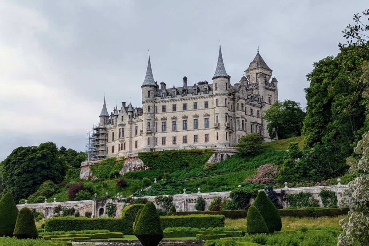 A grand, fairytale castle sits on a grassy mound in front of a lush green garden. Dunrobin Castle. 