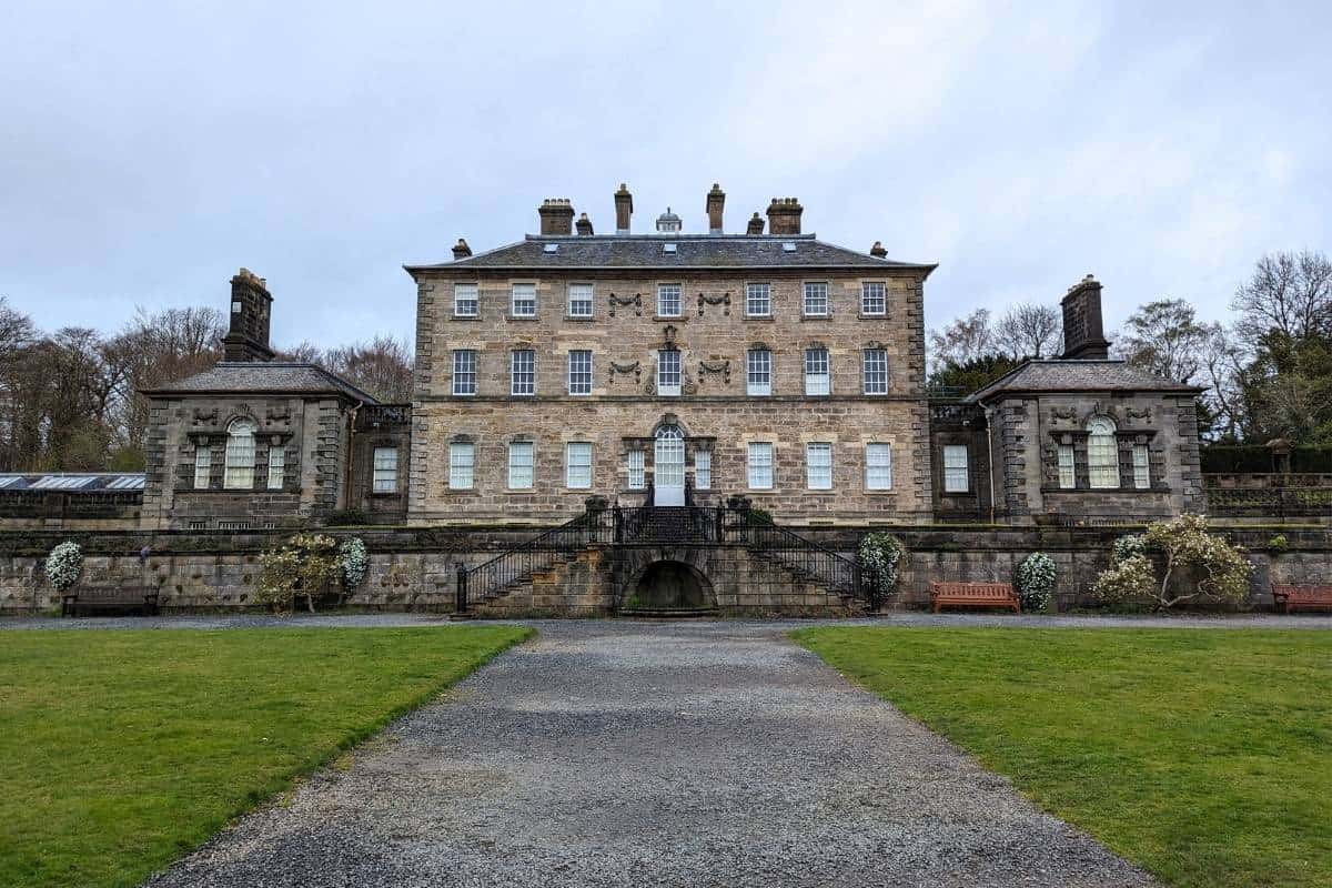 A grand house lined with windows and raised above the grass. Pollok House in Glasgow.