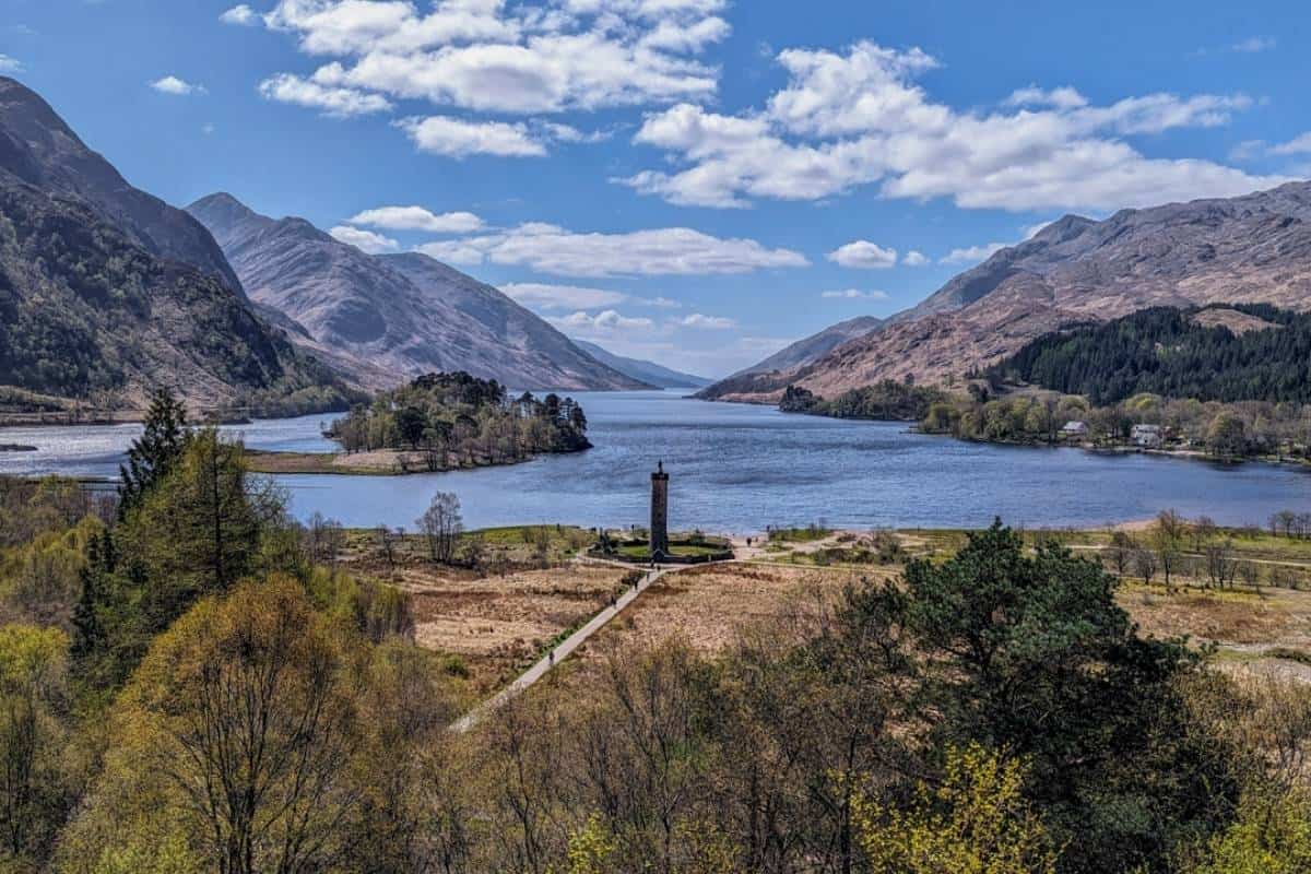 View of a monument set in front of a blue loch surrounded by rugged mountains. Glenfinnan in the Scottish Highlands, one of the most popular regions in Scotland. 