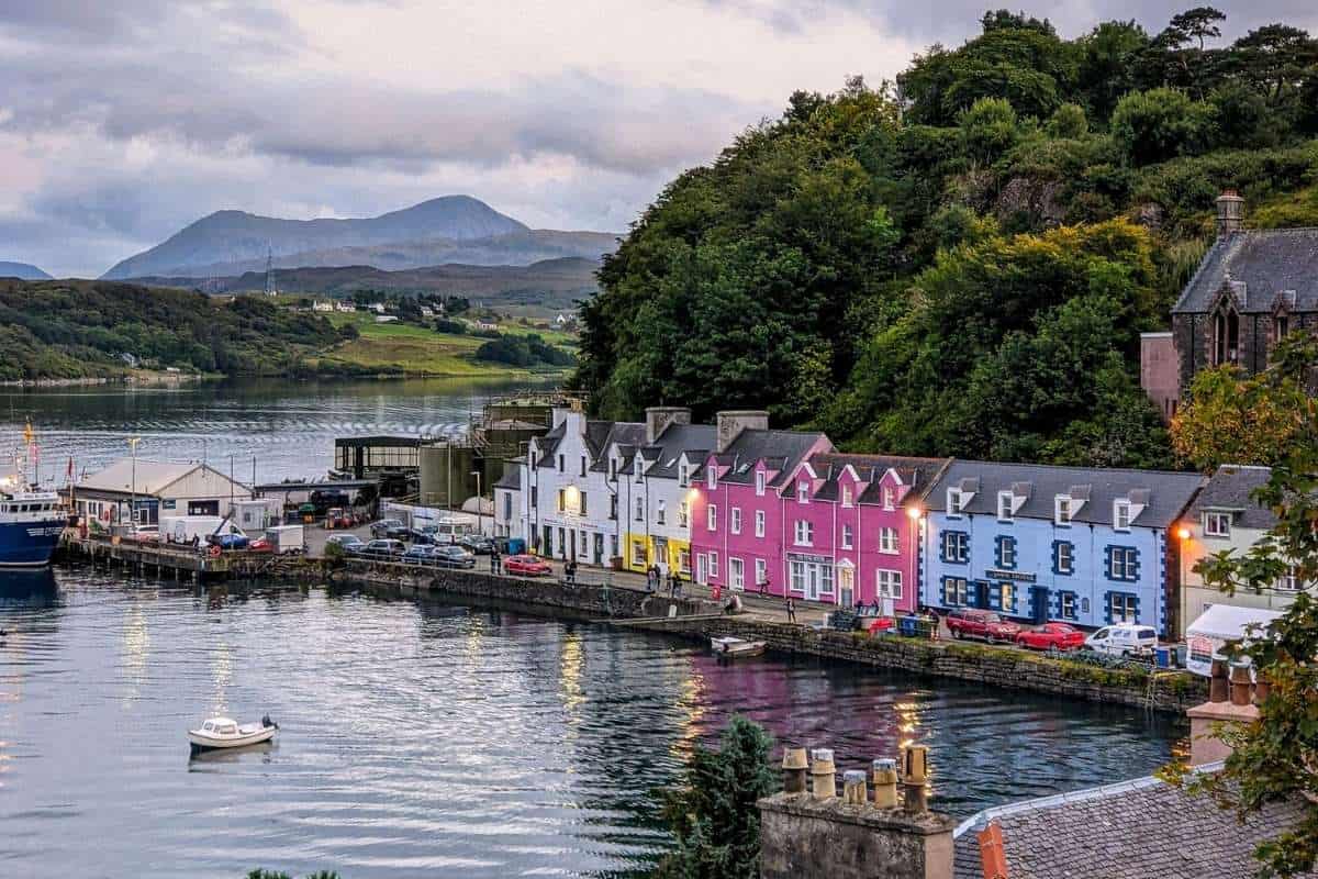 A colourful harbour with a blue and pink house are lit up in the evening light. Portree on the Isle of Skye. 
