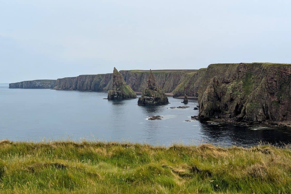 10 Easy Day Trips from Inverness Without a Car 18 Needle-sharp pinnacles rise from slate grey water in front of a long cliff. The DUncansby Sea STacks.