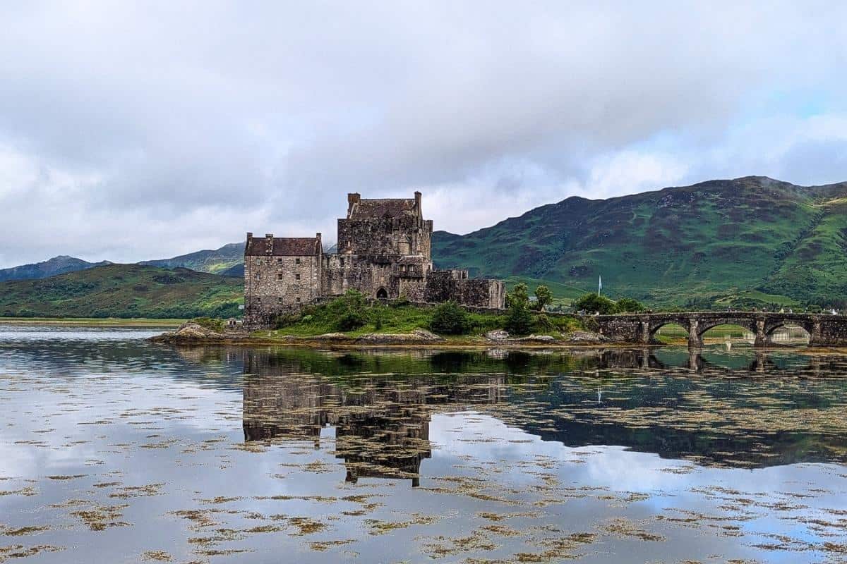 10 Easy Day Trips from Inverness Without a Car 13 A fortress sits on an island in a loch with a bridge running to the mainland. Green hills are behind it. EIlean Donan Castle.