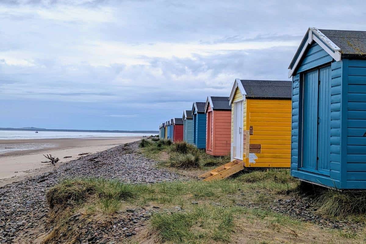 10 Easy Day Trips from Inverness Without a Car 11 Colourful beach huts line the grass with a long pale beach behind.
