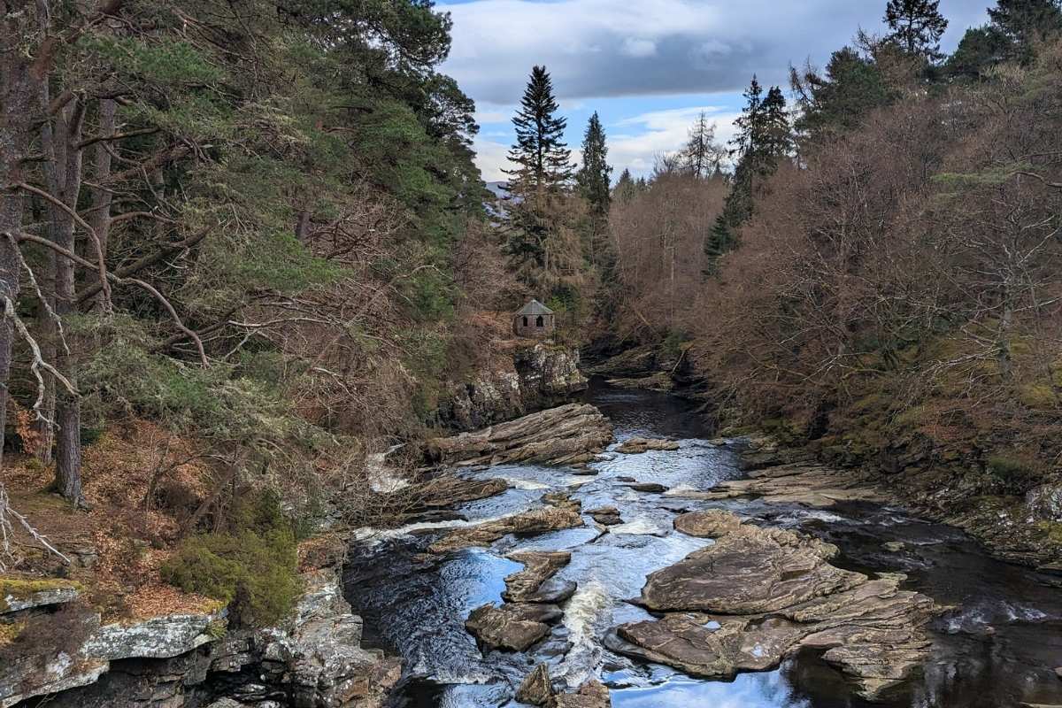10 Easy Day Trips from Inverness Without a Car 6 A river with rocks and rapids surrounded by pine trees. A little summerhouse sits on the riverbank. Invermoriston near Inverness.