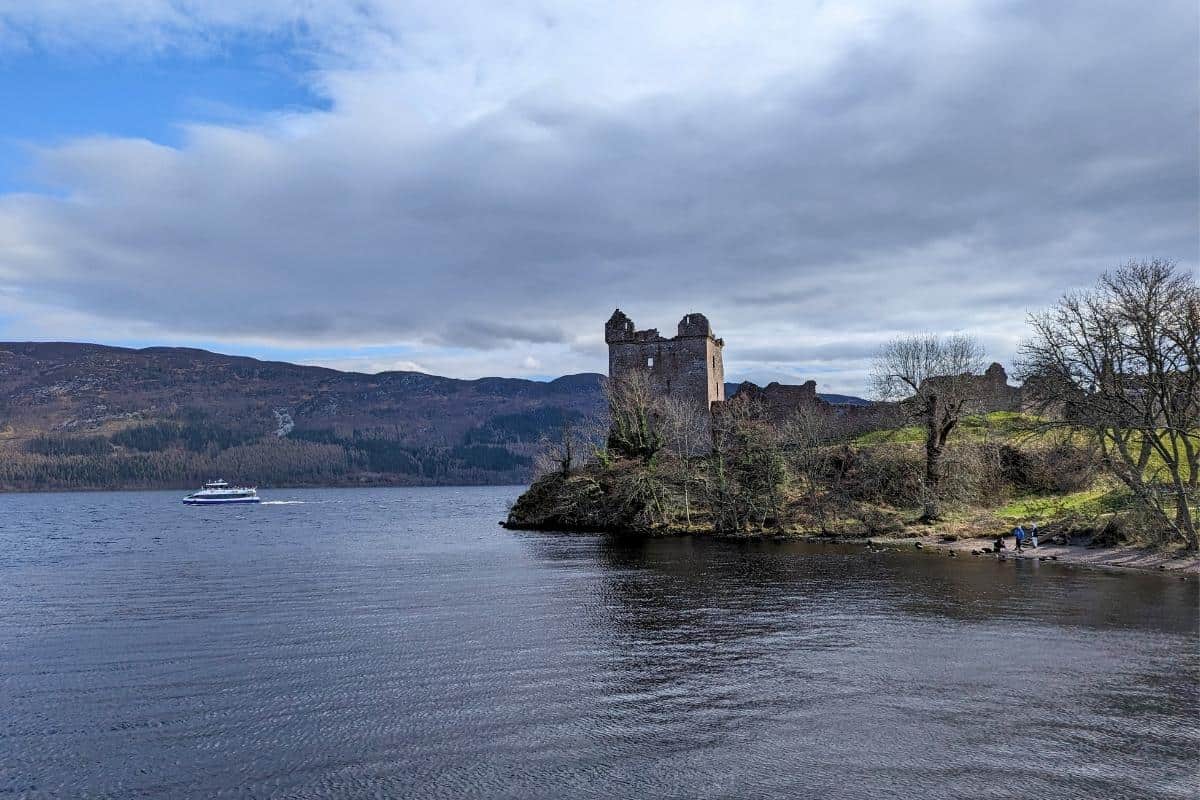 10 Easy Day Trips from Inverness Without a Car 5 A ruined castle sits by a loch surrounded by bare trees. A boat cruise is on the loch. Urquhart Castle near Inverness.