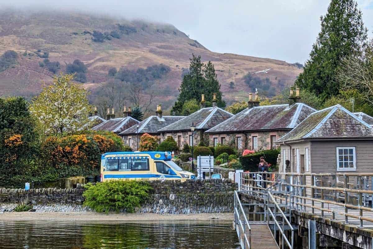 Village of Luss from the pier viewpoint on an overcast day. A retro ice cream van is at the front of the slate cottages for things to do in Luss, Scotland. 