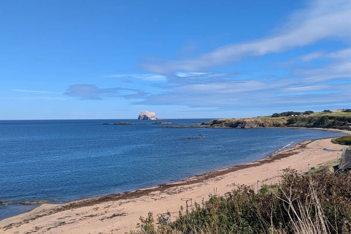 A large beach wraps around the headland with the silvery Bass Rock in the distance. 
