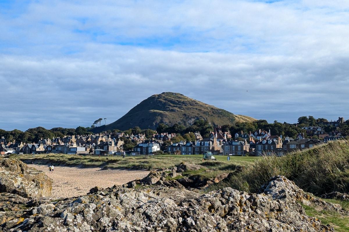 A large hill rises above houses with sunlight shining on it. The North Berwick Law. 