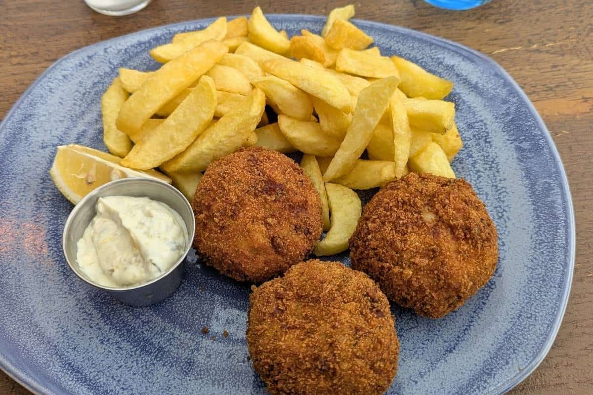 A pile of chips and three round fishcakes sit on a blue plate at The Rocketeer Restaurant. 