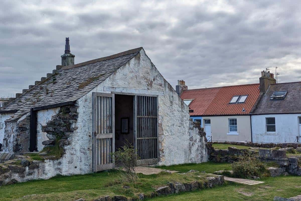 The ruins of an old chapel with colourful roofed buildings behind. St Andrew's Old Kirk is one of the best things to do in North Berwick.
