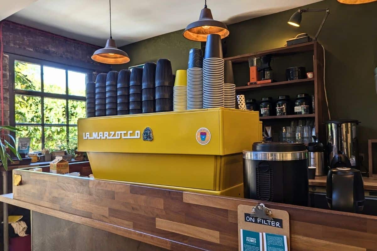 A yellow coffee machine piled high with mugs on a counter in a coffee bar. Steampunk Coffee Roaster. 