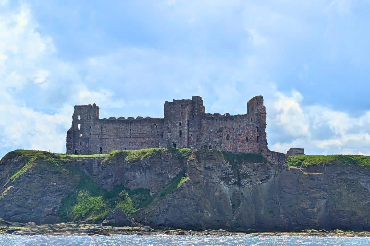The ruined thick walls of Tantallon Castle perched on clifftops on a sunny day. 