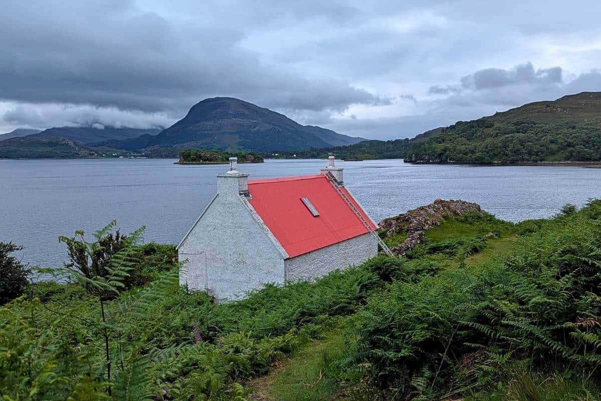 10 Easy Day Trips from Inverness Without a Car 16 A white cottage with a red roof sits in front of a loch in Applecross, one of the best day trips from Inverness with a tour.