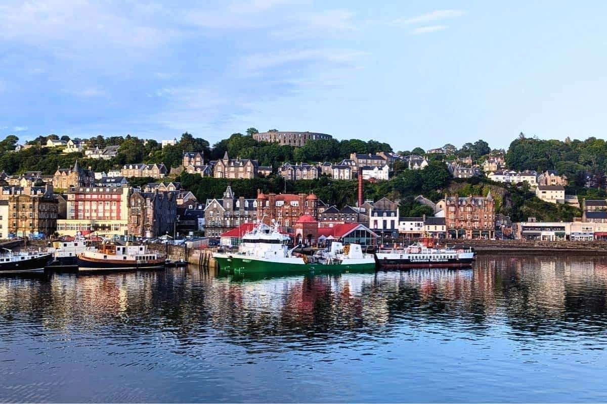 Where to Stay in Scotland Without a Car: Best Areas + Hotels 9 View of Oban from the water. Boats in the harbour and McCaig's Tower surrounded by trees on the hill above.