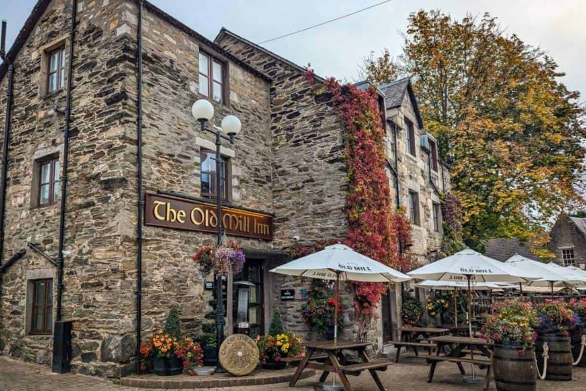 Where to Stay in Scotland Without a Car: Best Areas + Hotels 15 AN old stone building with the words 'The Old Mill Inn' on it. Benches with white umbrellas are outside in Pitlochry.